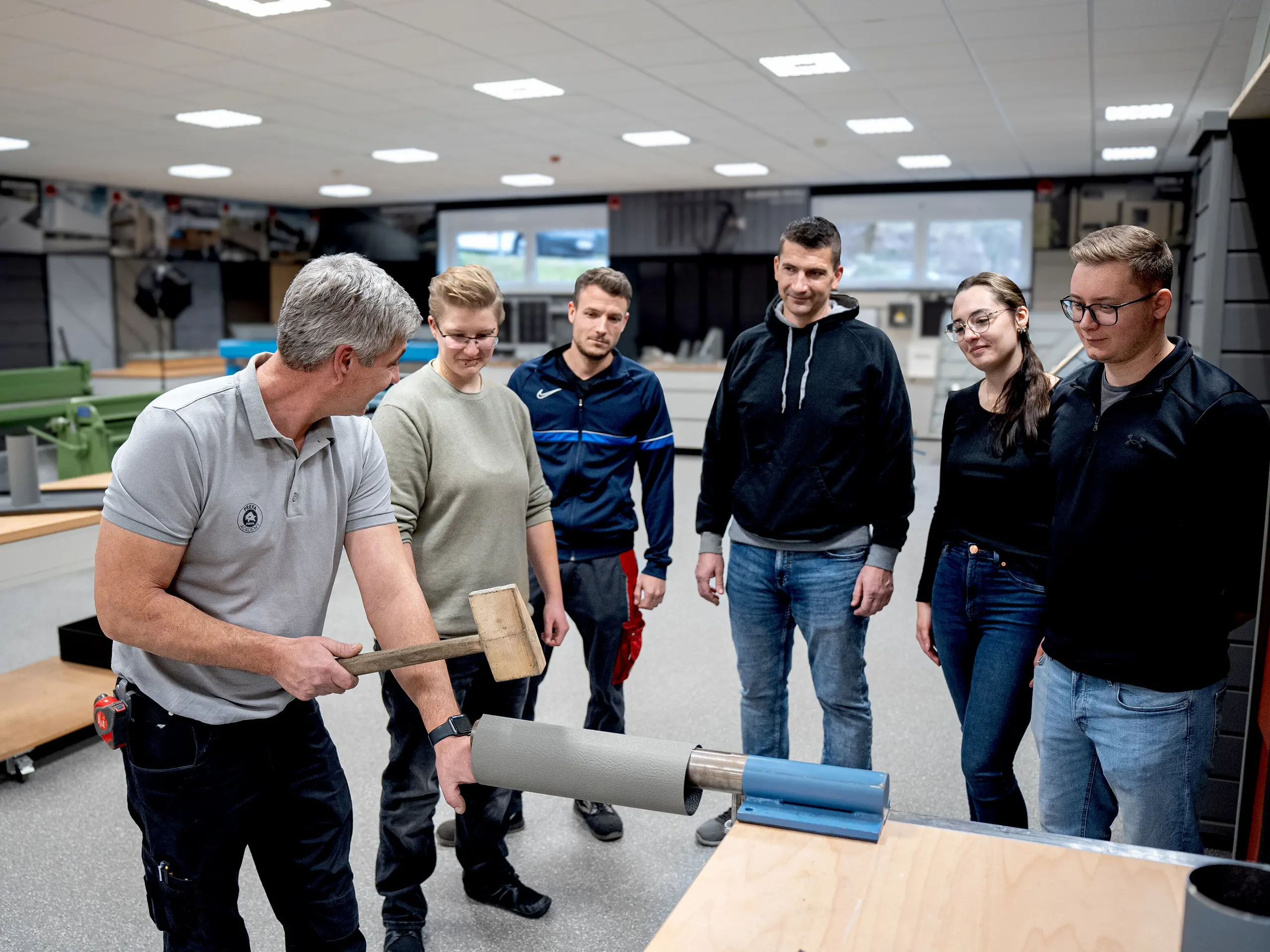 Praxisnahe Schulung in der PREFA Academy: Eine Gruppe junger Menschen verfolgt eine Live-Demonstration zur Verarbeitung von PREFA Aluminium. Im Mittelpunkt stehen Handwerk, Fachwissen und die hohe Verarbeitungsqualität der PREFA Systeme. 