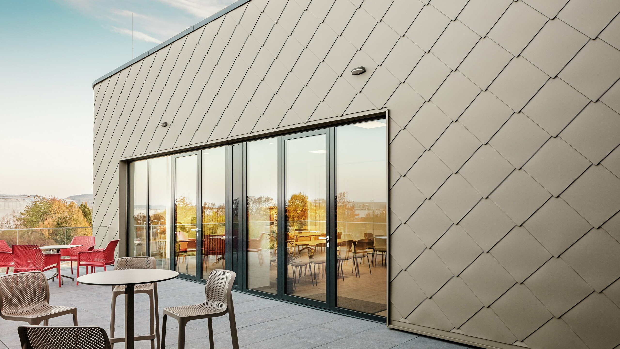 Die Fassade des neuen PREFA Standortes in Törökbálint besticht durch die eleganten PREFA Wandrauten 44 × 44 in P.10 Prefabronze. Die präzise verlegte Aluminiumfassade sorgt für ein modernes, dynamisches Erscheinungsbild und bietet gleichzeitig maximalen Schutz vor Witterungseinflüssen. Die großzügige Glasfront verbindet Innen- und Außenbereich und schafft auf der großzügigen Terrasse eine helle und einladende Atmosphäre.