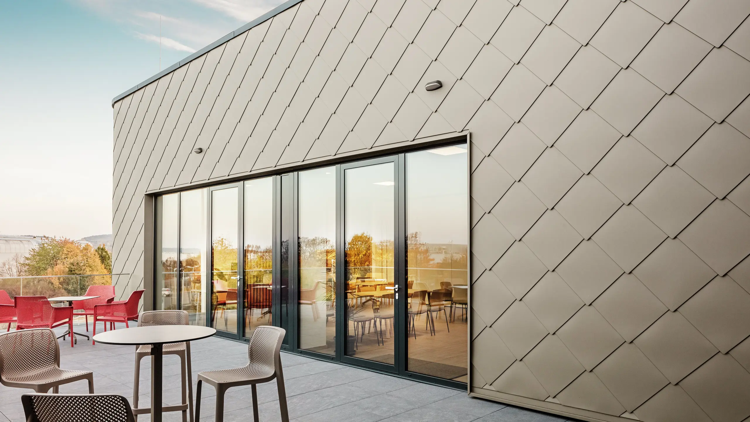 Die Fassade des neuen PREFA Standortes in Törökbálint besticht durch die eleganten PREFA Wandrauten 44 × 44 in P.10 Prefabronze. Die präzise verlegte Aluminiumfassade sorgt für ein modernes, dynamisches Erscheinungsbild und bietet gleichzeitig maximalen Schutz vor Witterungseinflüssen. Die großzügige Glasfront verbindet Innen- und Außenbereich und schafft auf der großzügigen Terrasse eine helle und einladende Atmosphäre.