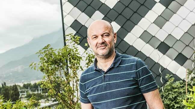 Portrait des Spenglers Patrick Gaide vor seinem Prestige Objekt mit der Aluminiumwandraute von PREFA in Python-Optik mit dunklem Polo Shirt