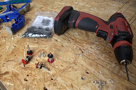 Zubehör für die Befestigung einer Aluminium-Verbundplatte auf einer Holz-Unterkonstruktion: Schrauben mit Gummidichtung, Festpunkthülsen, Akkuschrauber.