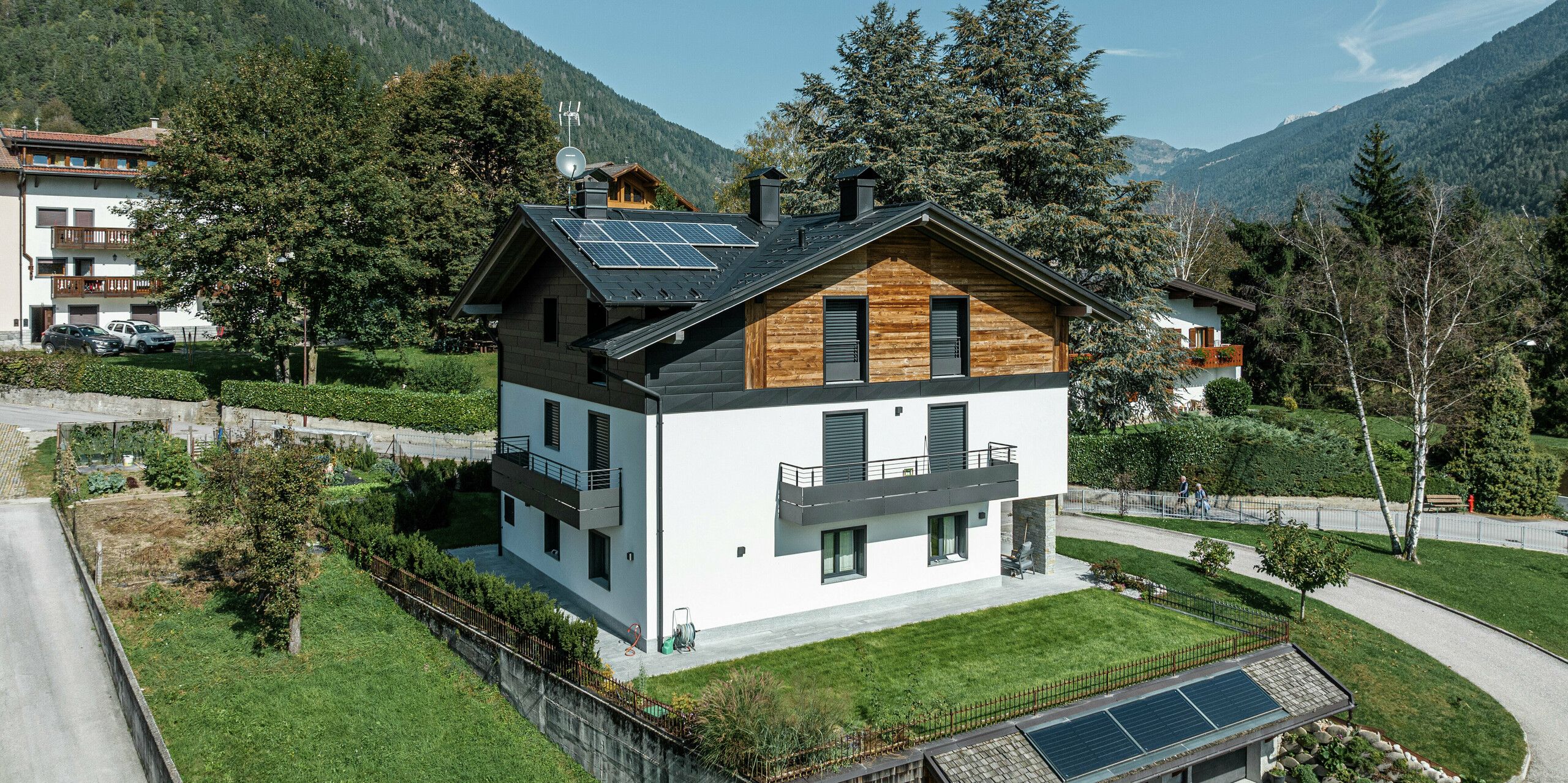 Modernisiertes Wohnhaus in Pelugo, Italien, mit PREFA Dachplatte R.16 in P.10 Anthrazit und PREFA Siding.X an der Fassade. Die Kombination von Aluminium, Holz und Putz sorgt für eine langlebige, witterungsbeständige und stilvolle Architektur in alpiner Umgebung. Solarmodule auf dem Dach und der Garage runden das nachhaltige Energiekonzept ab.