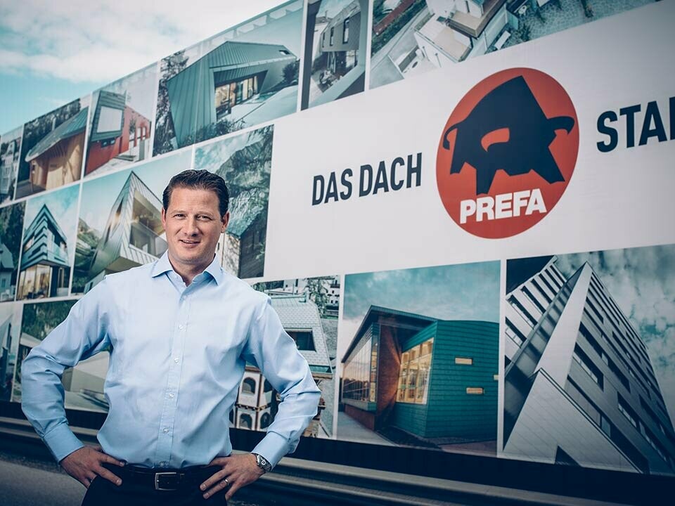 PREFA Geschäftsführer, Leopold Pasquli, vor dem Firmengebäude mit PREFA Logo.