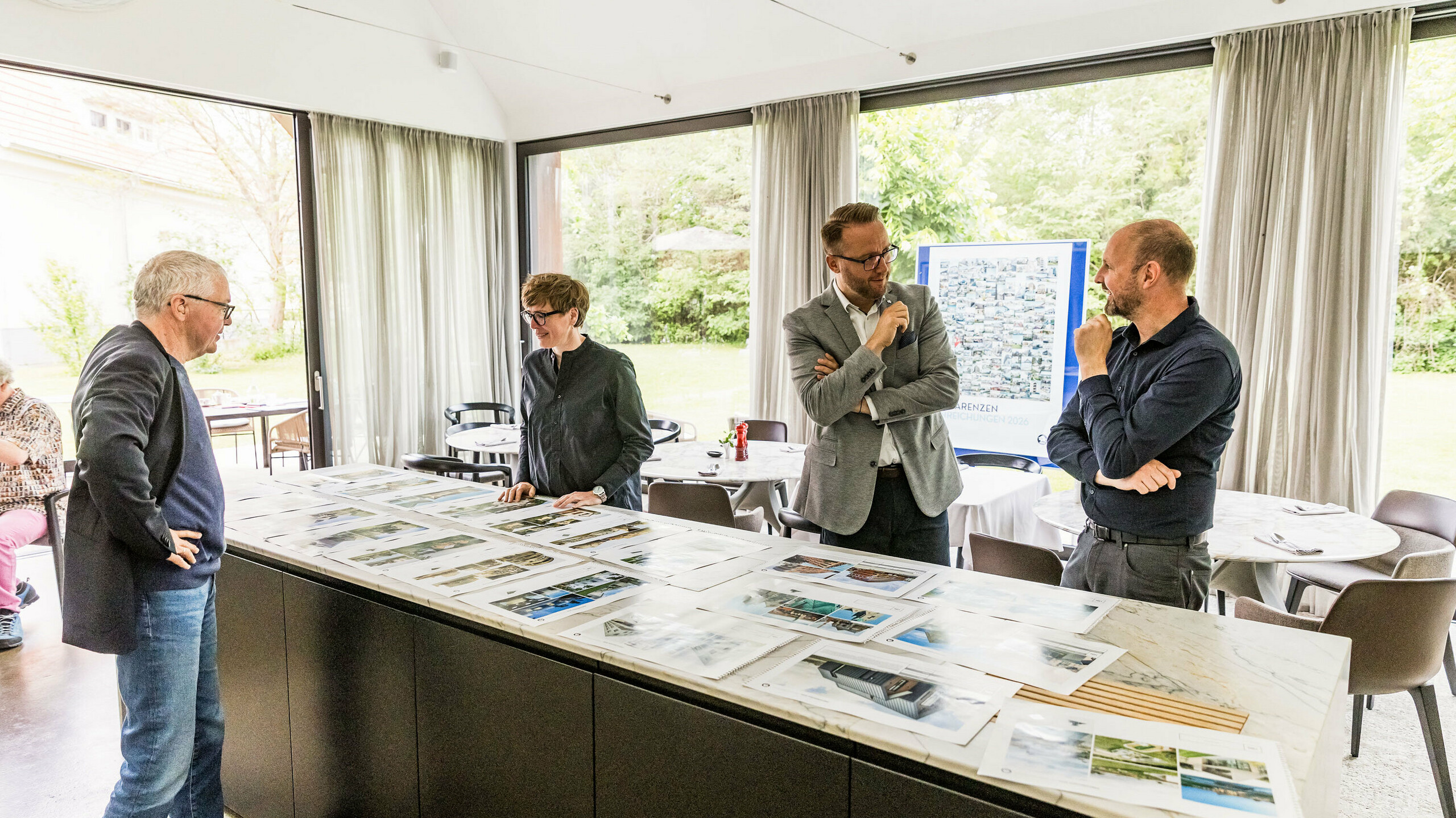 Die finale Auswahl der PREFARENZEN Architekturhighlights für 2026 liegt auf großen Bildern vor Teilen der hochkarätig besetzten Jury. Die Experten prüfen die eingereichten Architekturprojekte sorgfältig auf Innovationskraft, gestalterische Qualität und den Einsatz von PREFA-Materialien. Die Sitzung in der lichtdurchfluteten Winzerresidenz im burgenländischen Seewinkel bildet den Abschluss des intensiven Juryprozesses für das PREFARENZEN-Architekturbuch und den Kalender 2026.
