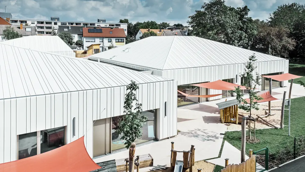 Zu sehen ist hier der Kindergarten in Niederwerrn, eingedeckt mit dem Prefalz Dachsystem von PREFA, mit Ansicht in den Garten.