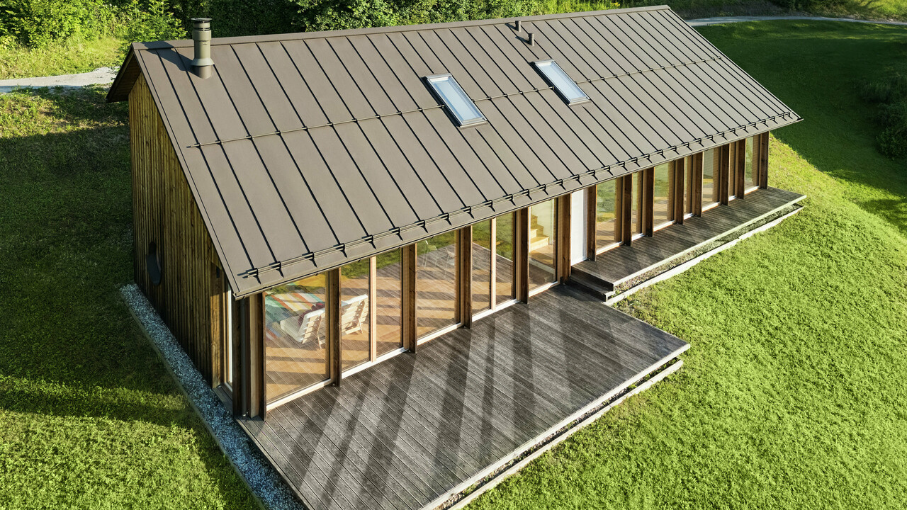 Ein modernes Holzhaus mit großzügiger Glasfassade und einem robusten PREFALZ-Aluminiumdach in der Farbe P.10 Braun – ideal für Hanglagen wie in Vinje. Die hochwertige Dachdeckung garantiert maximale Witterungsbeständigkeit, lange Lebensdauer und eine elegante Optik. Präzise gesetzte Stehfalze und integrierte Dachfenster schaffen ein luftiges und nachhaltiges Wohnkonzept. Die präzise Verarbeitung der Aluminium-Stehfalze wird aus der Vogelperspektive sichtbar.