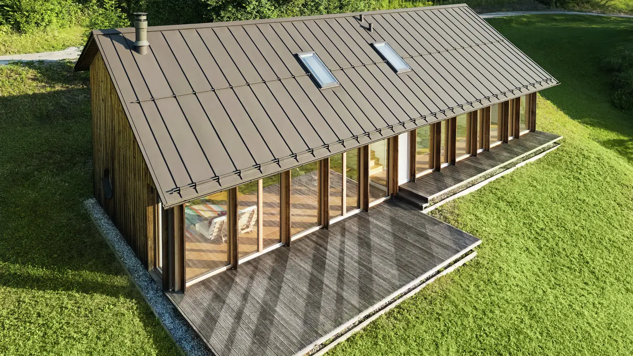Ein modernes Holzhaus mit großzügiger Glasfassade und einem robusten PREFALZ-Aluminiumdach in der Farbe P.10 Braun – ideal für Hanglagen wie in Vinje. Die hochwertige Dachdeckung garantiert maximale Witterungsbeständigkeit, lange Lebensdauer und eine elegante Optik. Präzise gesetzte Stehfalze und integrierte Dachfenster schaffen ein luftiges und nachhaltiges Wohnkonzept. Die präzise Verarbeitung der Aluminium-Stehfalze wird aus der Vogelperspektive sichtbar.