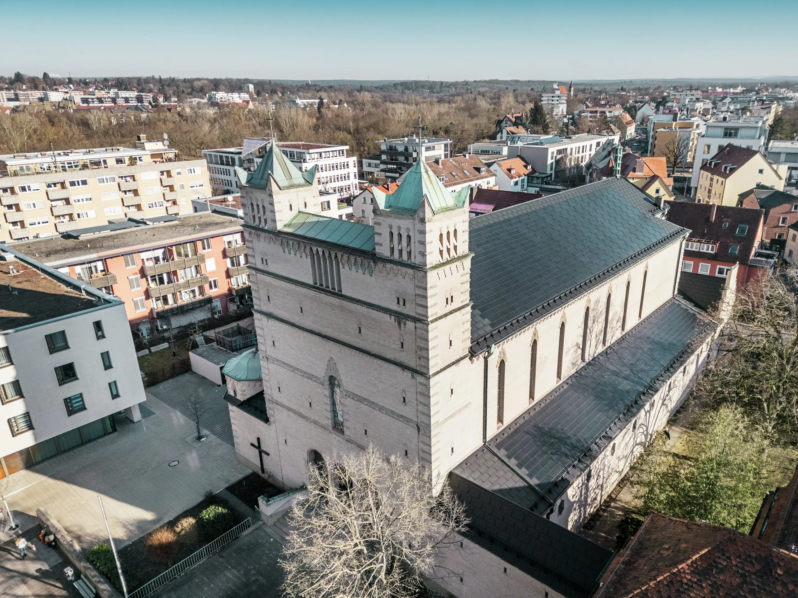 Vorderseite der St. Karl Borromäus Kirche in Nürnberg: Das Bild zeigt das beeindruckende Dach der denkmalgeschützten Kirche, das mit schwarzen PREFA-Solardachplatten gedeckt ist. Die Solarmodule fügen sich harmonisch in die historische Architektur der Kirche ein und stellen gleichzeitig eine moderne Lösung zur nachhaltigen Energiegewinnung dar. Im Hintergrund sind moderne Gebäude und die grünen Hügel Nürnbergs zu sehen, was den gelungenen Übergang zwischen traditioneller Kirchenarchitektur und zeitgemäßer Energieversorgung verdeutlicht. Das Aluminiumdach der Kirche wird durch die stilvolle PREFA Dachplatte R.16 vervollständigt.