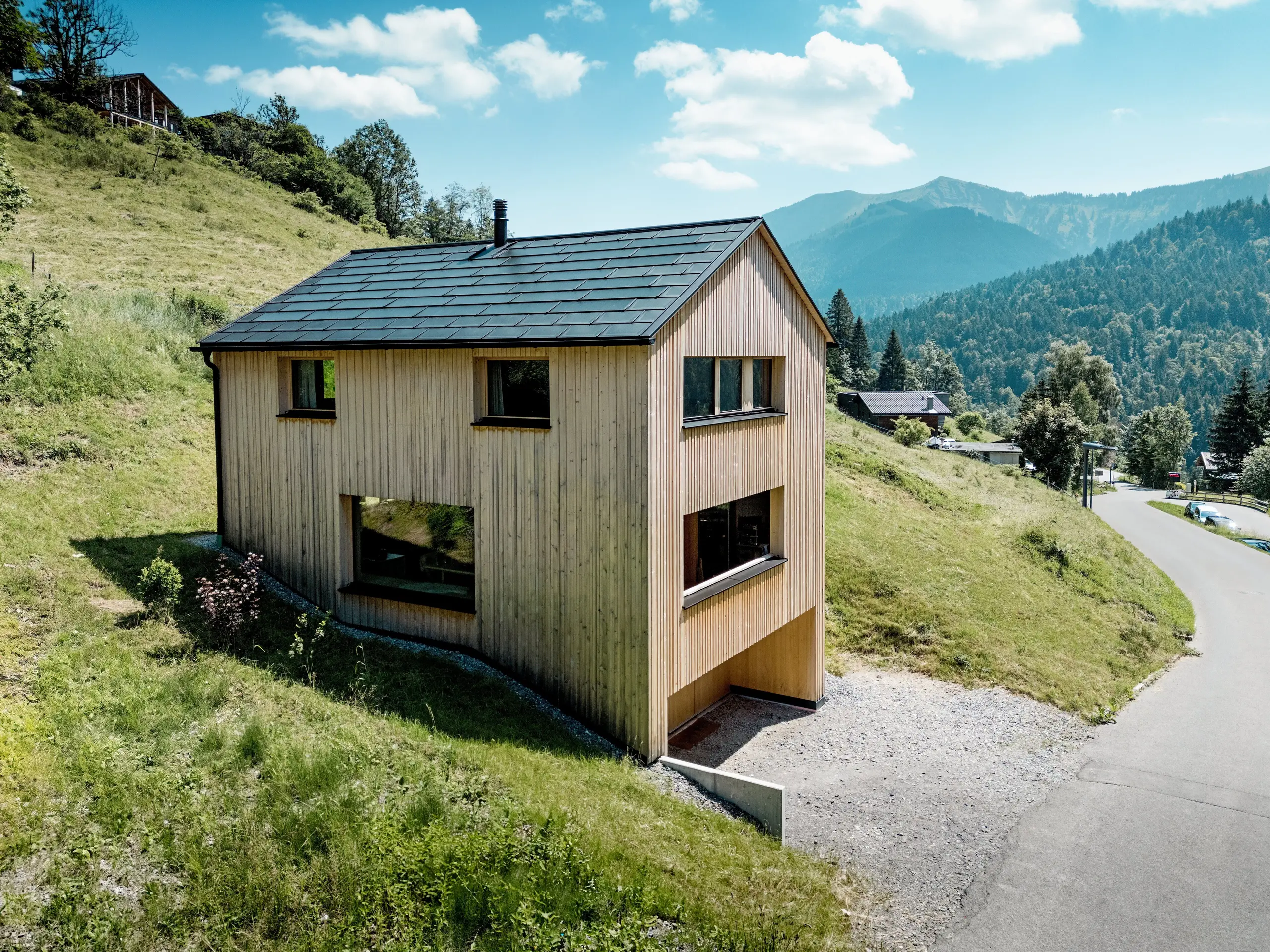 Hoch über dem Tal steht Haus Immi wie ein klarer Holzmonolith im sonnigen Berghang von Ebnit. Die reduzierte Weißtannenfassade und das schwarze PREFA Solardach setzen einen kraftvollen Kontrast zur weiten Alpenlandschaft. Integrierte Solardachplatten und Dachplatten R.16 in P.10 Schwarz liefern Solarstrom, trotzen alpinem Wetter und sichern ein langlebiges, harmonisches Dachbild.