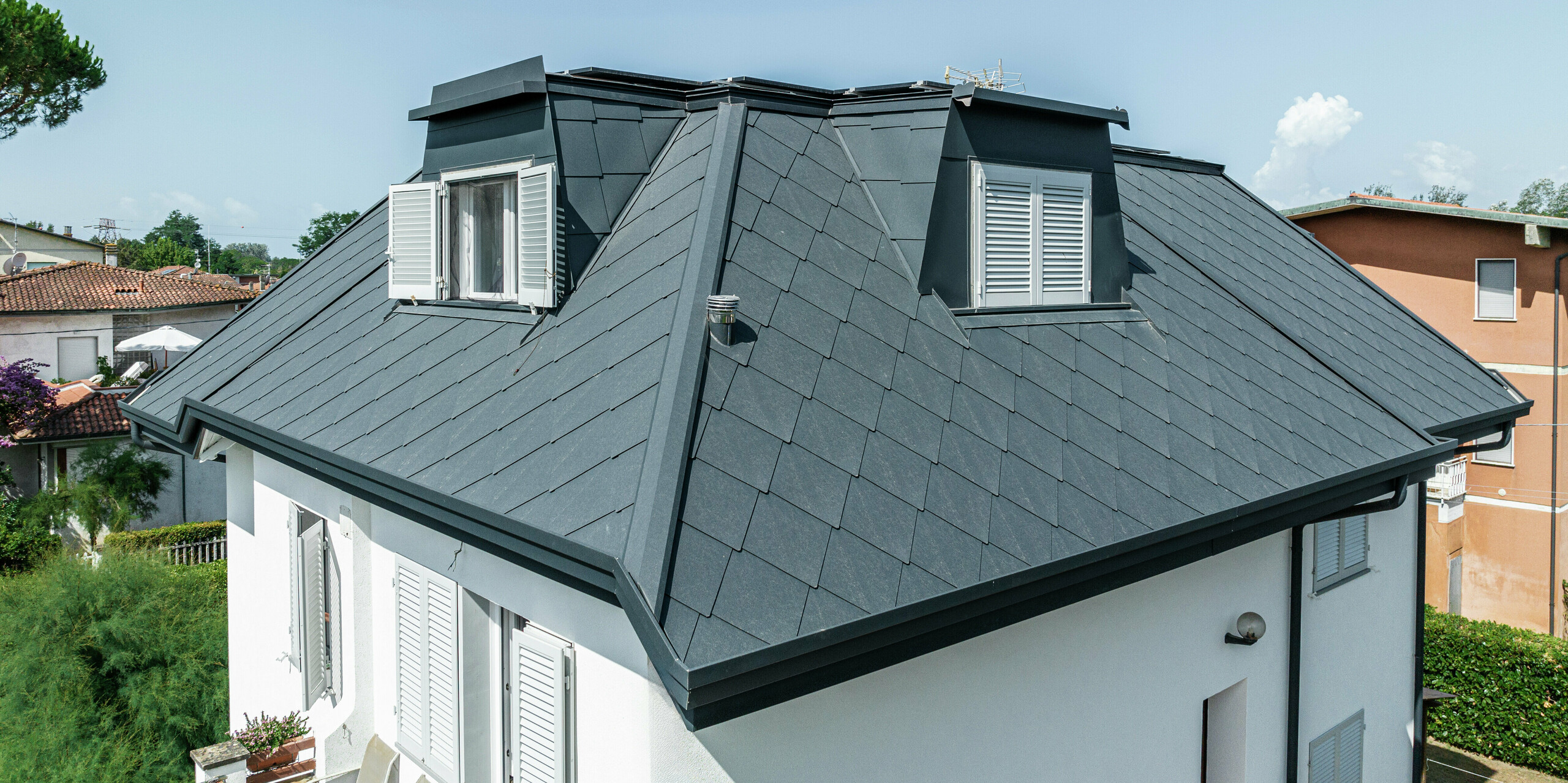 Die präzise Verarbeitung der PREFA Dachraute 44 × 44 in P.10 Steingrau am Einfamilienhaus in Montignoso ist in dieser Nahaufnahme deutlich zu erkennen. Die hochwertige Aluminiumdeckung sorgt für eine stilvolle, moderne Optik und bietet gleichzeitig höchste Widerstandsfähigkeit gegen extreme Witterungseinflüsse. Die formschönen Gauben fügen sich harmonisch in das Dach ein und schaffen zusätzlichen Wohnraum unter der robusten und langlebigen Dacheindeckung. Ein perfektes Zusammenspiel von Design und Funktionalität.