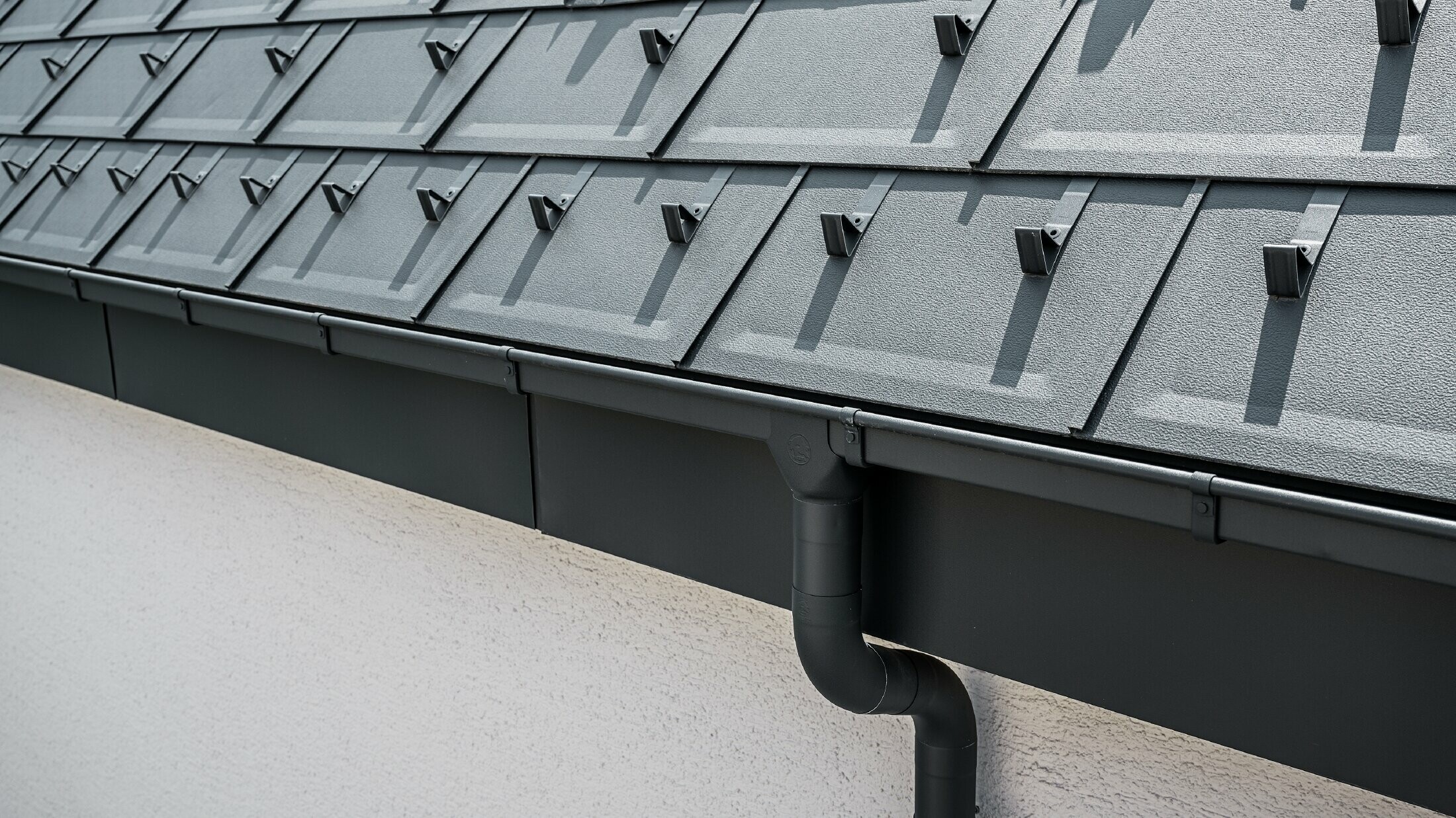 Steile Dachfläche eingedeckt mit der Dachplatte R.16 mit eckiger PREFA Kastenrinne mit Rinnenkessel und Ablaufrohr in Anthrazit