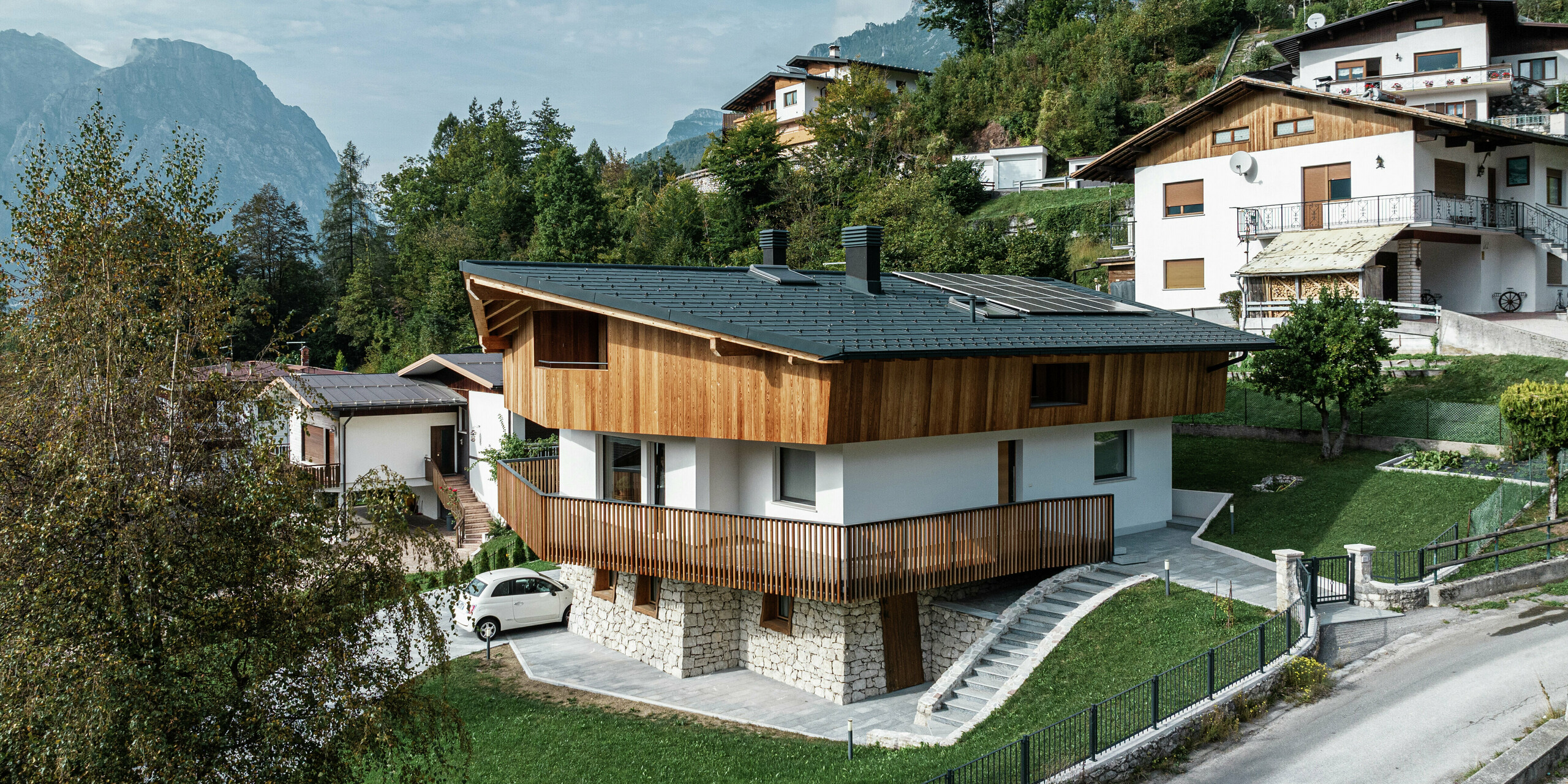 Sanierungsprojekt in Agordo, Italien: Ein Einfamilienhaus wurde mit einem widerstandsfähigen PREFA Aluminiumdach in P.10 Anthrazit neu eingedeckt. Die PREFA Dachplatte R.16 schützt zuverlässig vor extremen Witterungseinflüssen und sorgt für eine stilvolle Optik. Die PREFA Dachentwässerung mit Kastenrinne und Ablaufrohr sorgt zudem für eine effiziente Wasserableitung. Die Kombination aus naturbelassener Holzfassade, weißer Putzfassade und robustem Aluminiumdach fügt sich harmonisch in die alpine Umgebung ein.