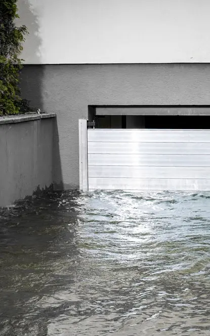 Garageneinfahrt in den Keller mit einem Garagentor das geschützt wird durch den PREFA Hochwasserschutz. Die Einfahrt ist voller Wasser.