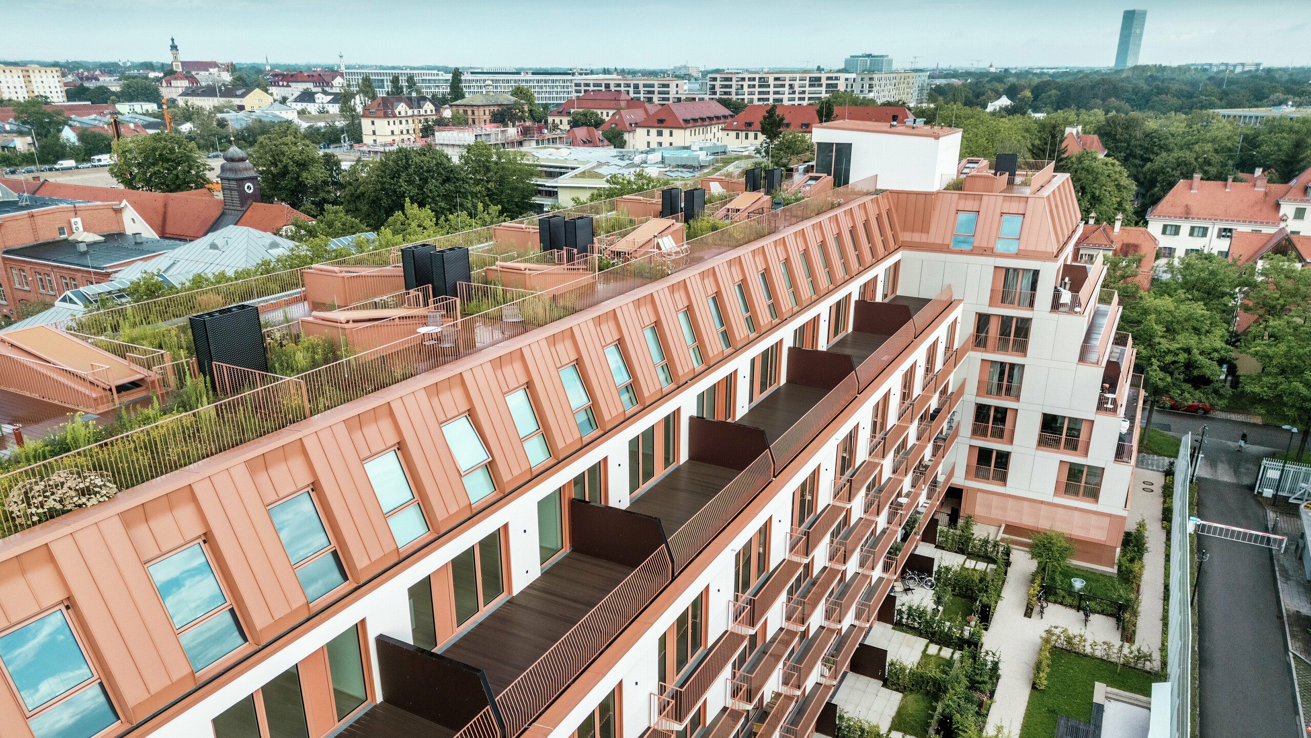 Luftaufnahme des Wohnprojektes Van B in München mit dem markanten PREFALZ Aluminiumdach in der Sonderfarbe IGP Orange HDP von PREFA. Großzügige Balkone, begrünte Dachterrassen und eine präzise Fassadengestaltung unterstreichen das durchdachte architektonische Konzept. Ideal für nachhaltige Stadtentwicklung und urbanes Wohnen mit hoher Lebensqualität und ästhetischem Anspruch.