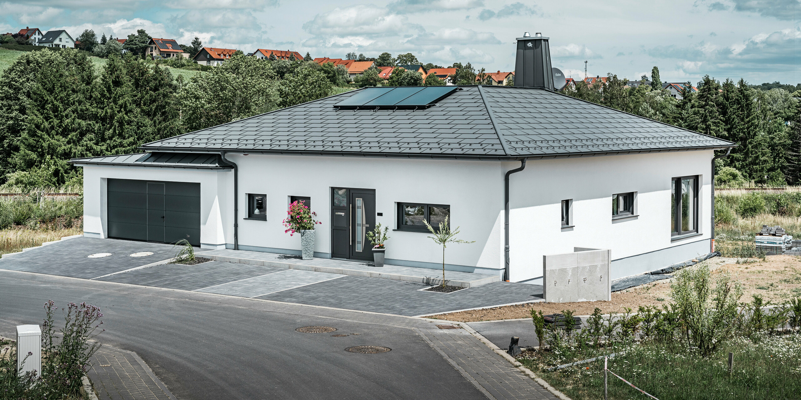 PREFA Dachplatte R.16 und PREFALZ sowie Ablaufrohr und Hängerinne in P.10 Dunkelgrau auf dem Dach eines Bungalows