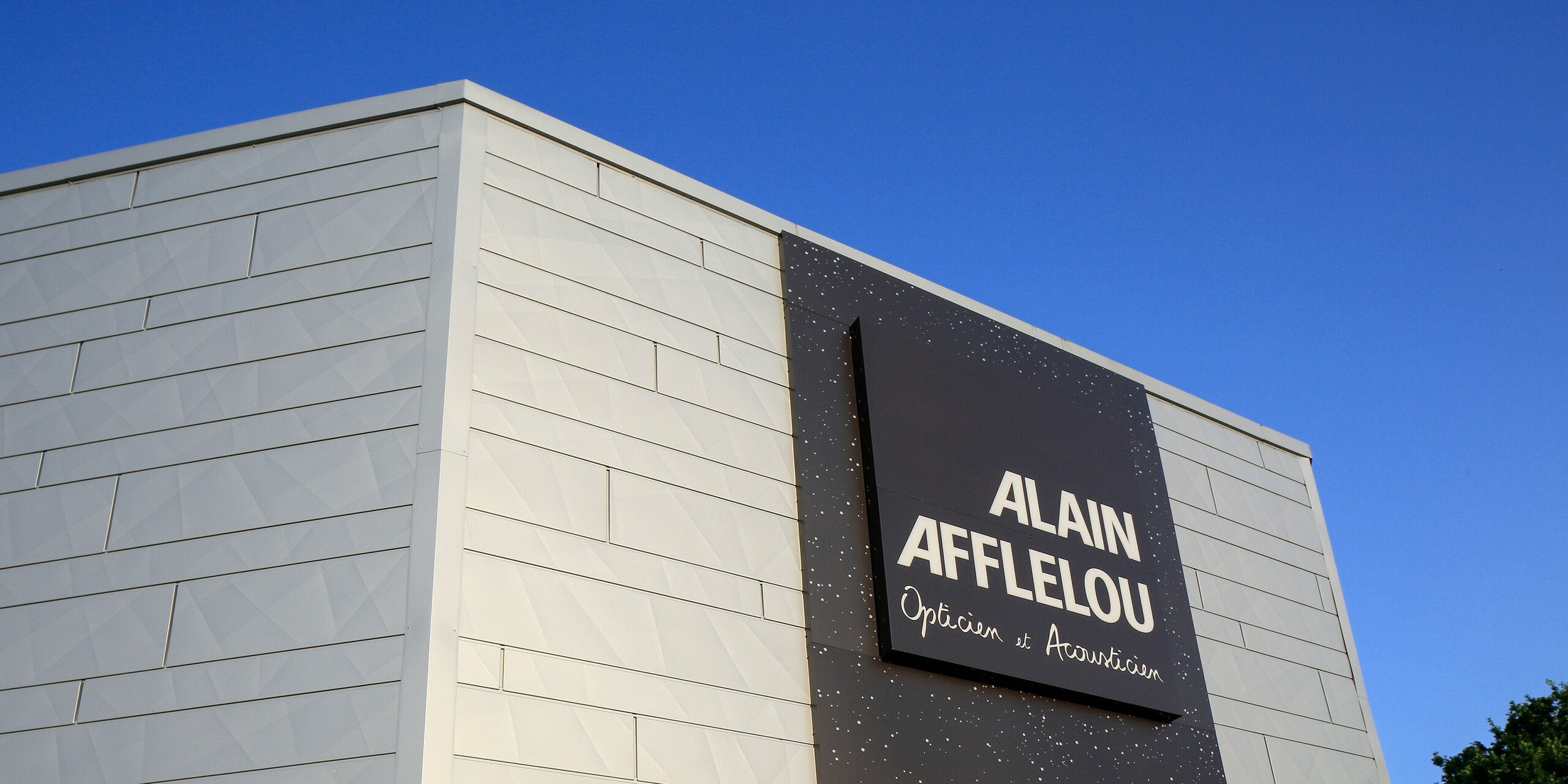 Eingangsbereich des Optik- und Akustik-Shops AFFLELOU in Auray mit großem Firmenschild und einer extravaganten Fassade bestehend aus PREFA Siding.X in Silbermetallic