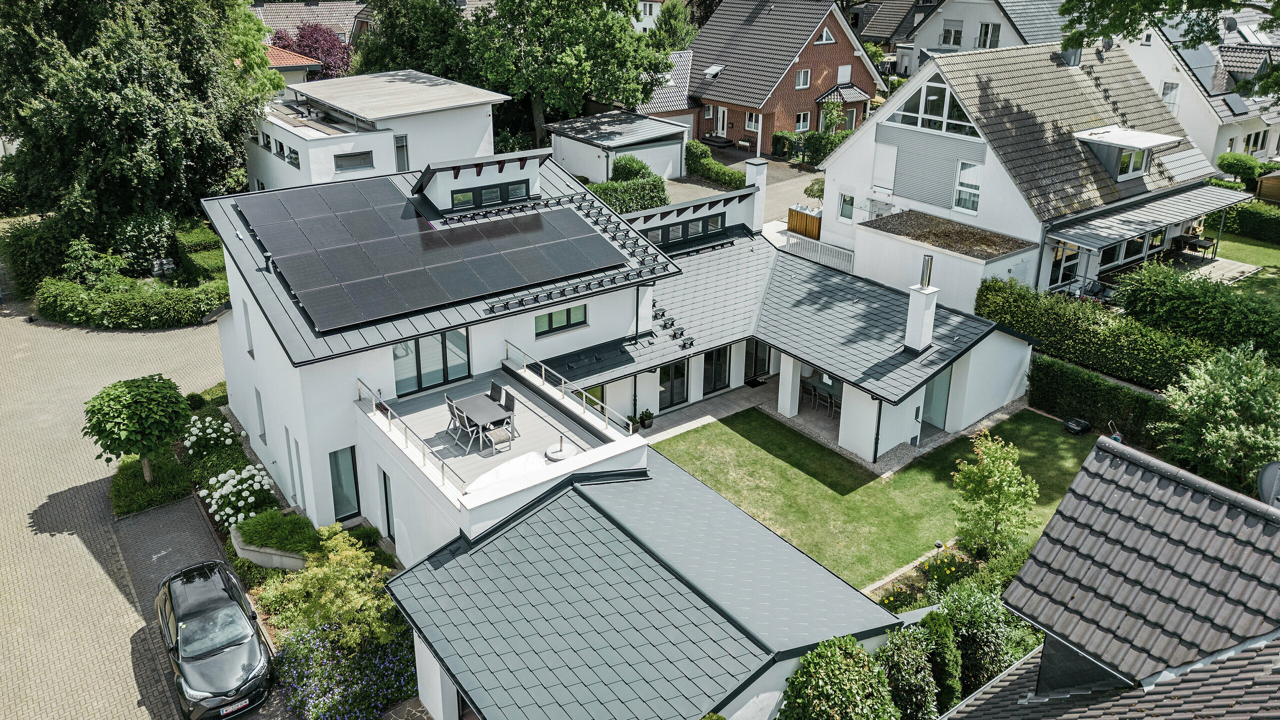 Vogelperspektive auf die herausragende Dachlandschaft eines Einfamilienhauses in Dortmund mit PREFA Dachschindeln DS.19 und PREFALZ in P.10 Anthrazit sowie einer großflächigen PV-Anlage