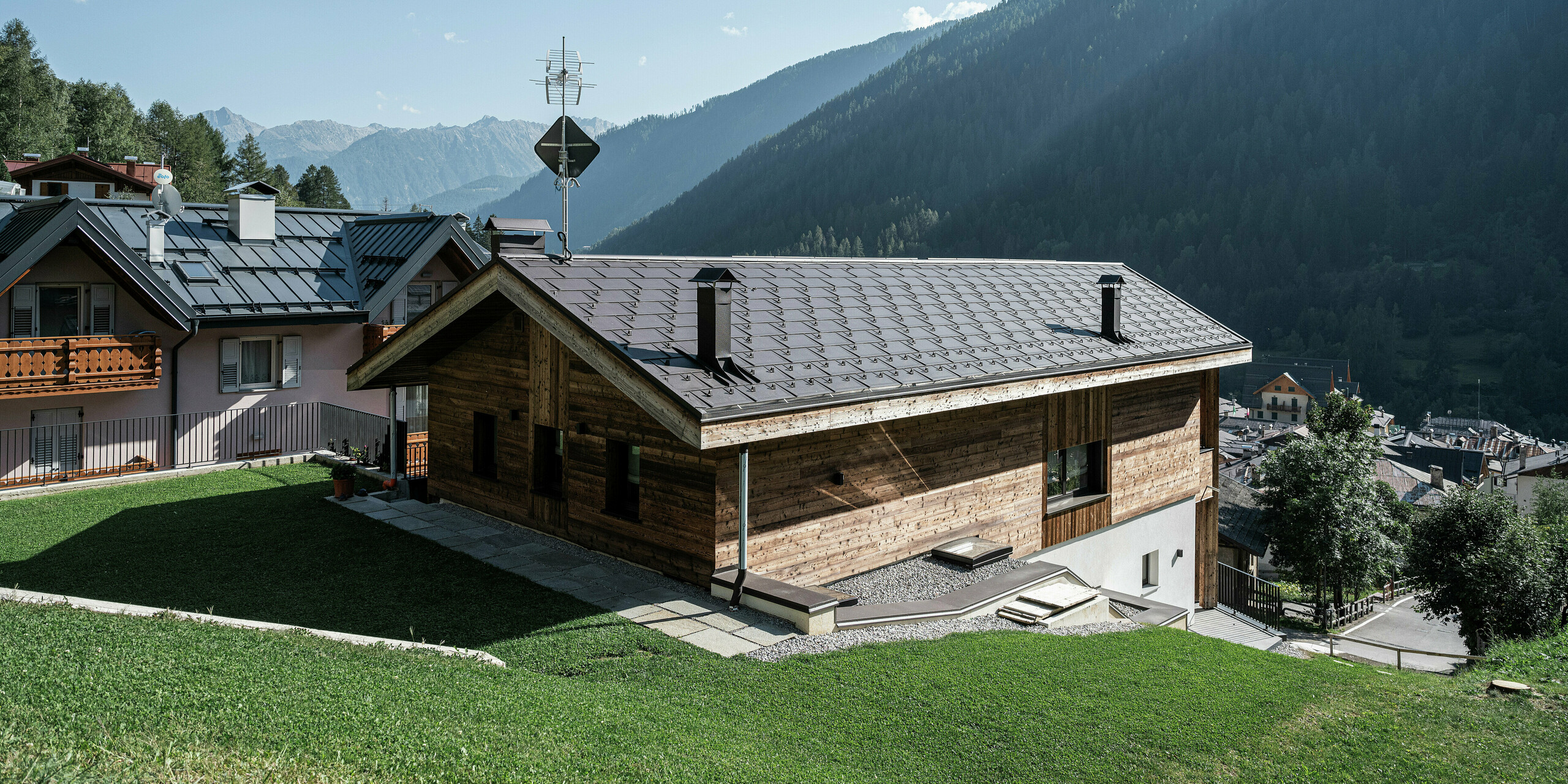 Rückseite eines modernen Berghauses in Cogolo, im italienischen Val di Sol, mit langlebigen PREFA Dachplatten R.16 in P.10 Braun. Das robuste Aluminiumdach fügt sich perfekt in die alpine Landschaft ein und schützt das Gebäude zuverlässig vor Schnee, Wind und Wetter. Klare Linien und höchste Belastbarkeit machen dieses Dach zur idealen Lösung für hochgelegene Regionen.