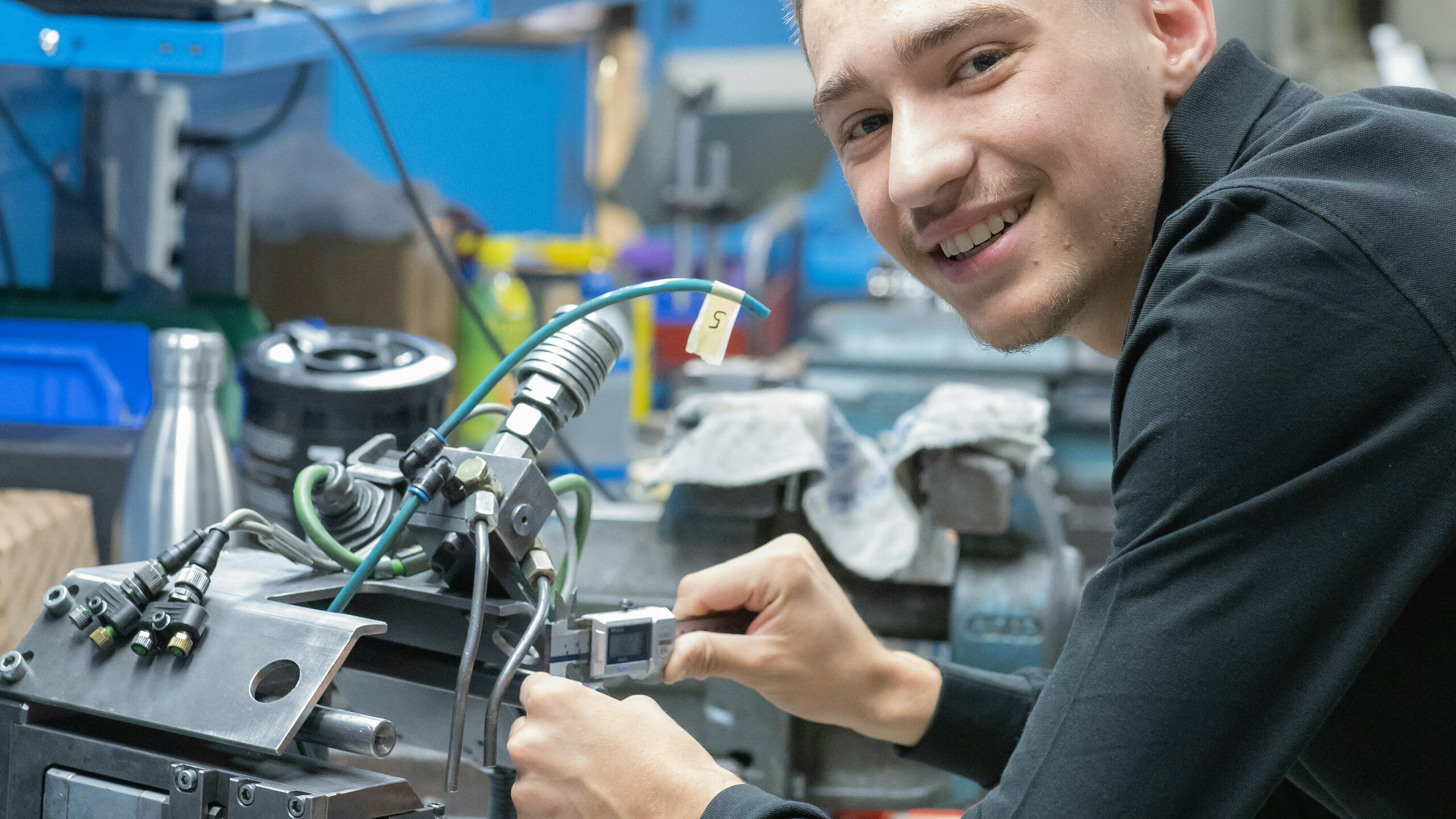 PREFA Lehrling im Portrait: er lächelt in die Kamera, während er an einer Produktions-Maschine arbeitet.