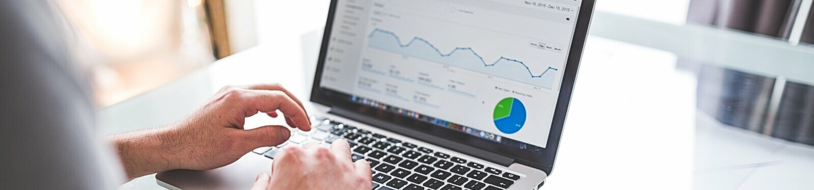 Eine Person, die an einem Laptop arbeitet, auf dessen Bildschirm grafische Darstellungen von Statistiken und ein Kuchendiagramm zu sehen sind, was auf die Durchführung von Online-Marketing-Aktivitäten hindeutet