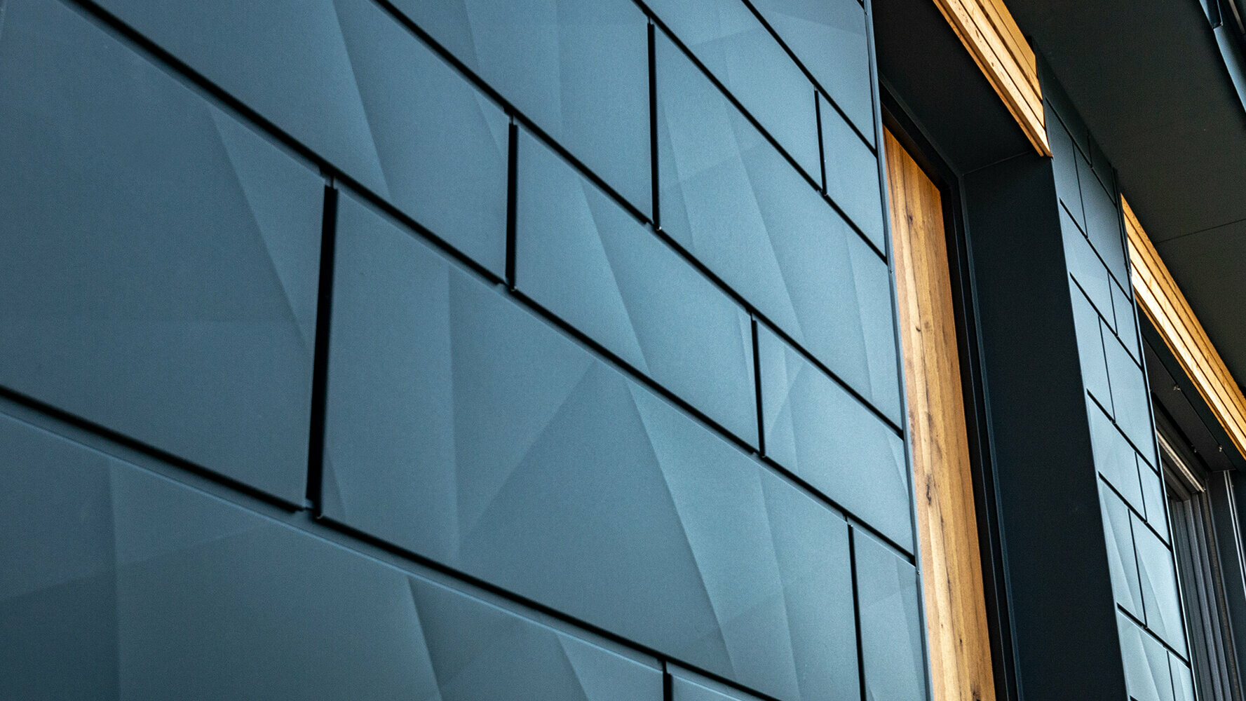 PREFA Fassadenpaneele mit geknickter Optik; PREFA Aluminium Siding.X in Anthrazit mit Holzfassade kombiniert.