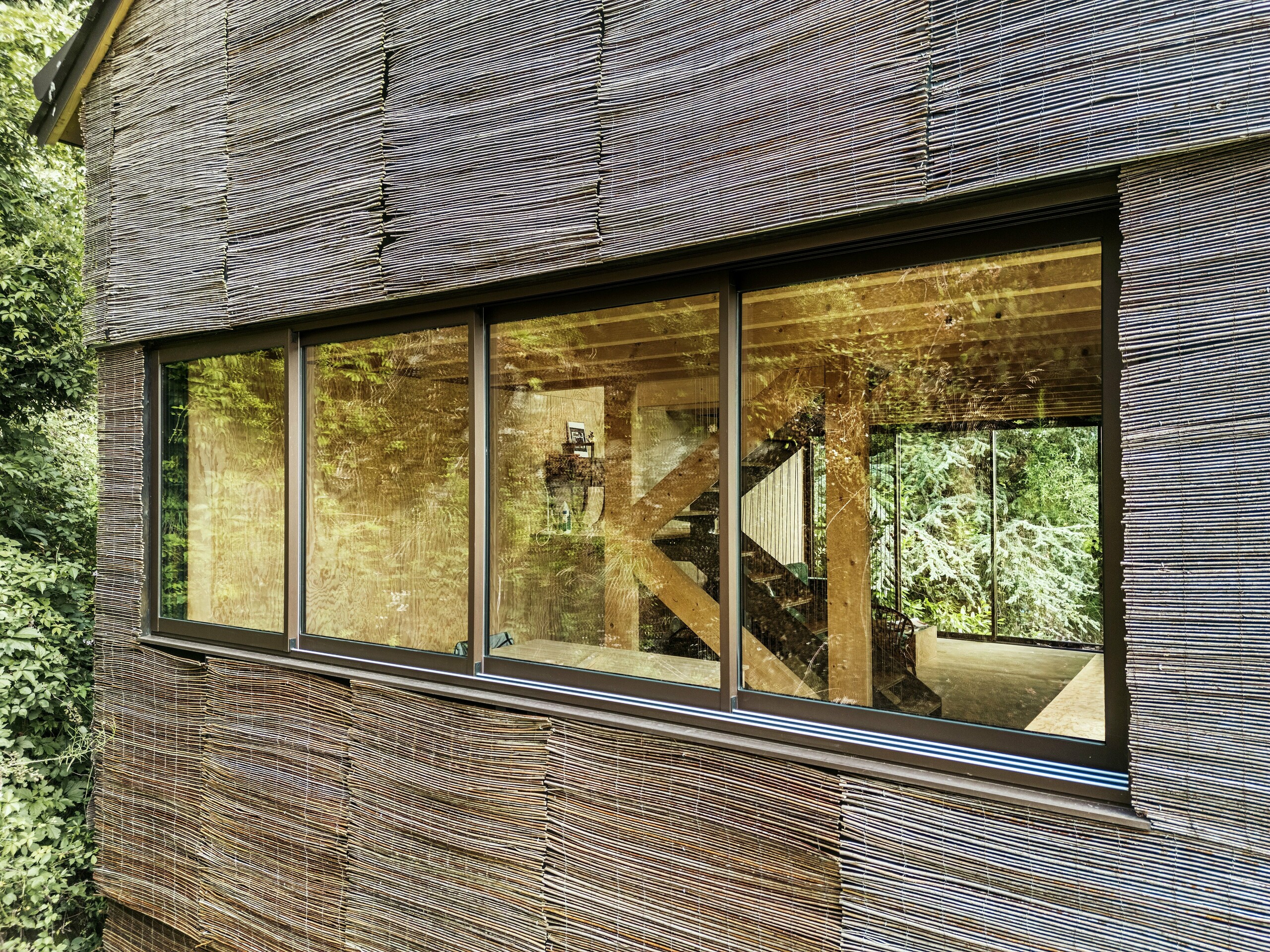 Detailaufnahme eines Fensters mit modernem Aluminiumrahmen und Weidenfassade bei einem Haus in Frankreich – nachhaltiges Design mit PREFA Dachschindeln und natürlicher Umgebung.