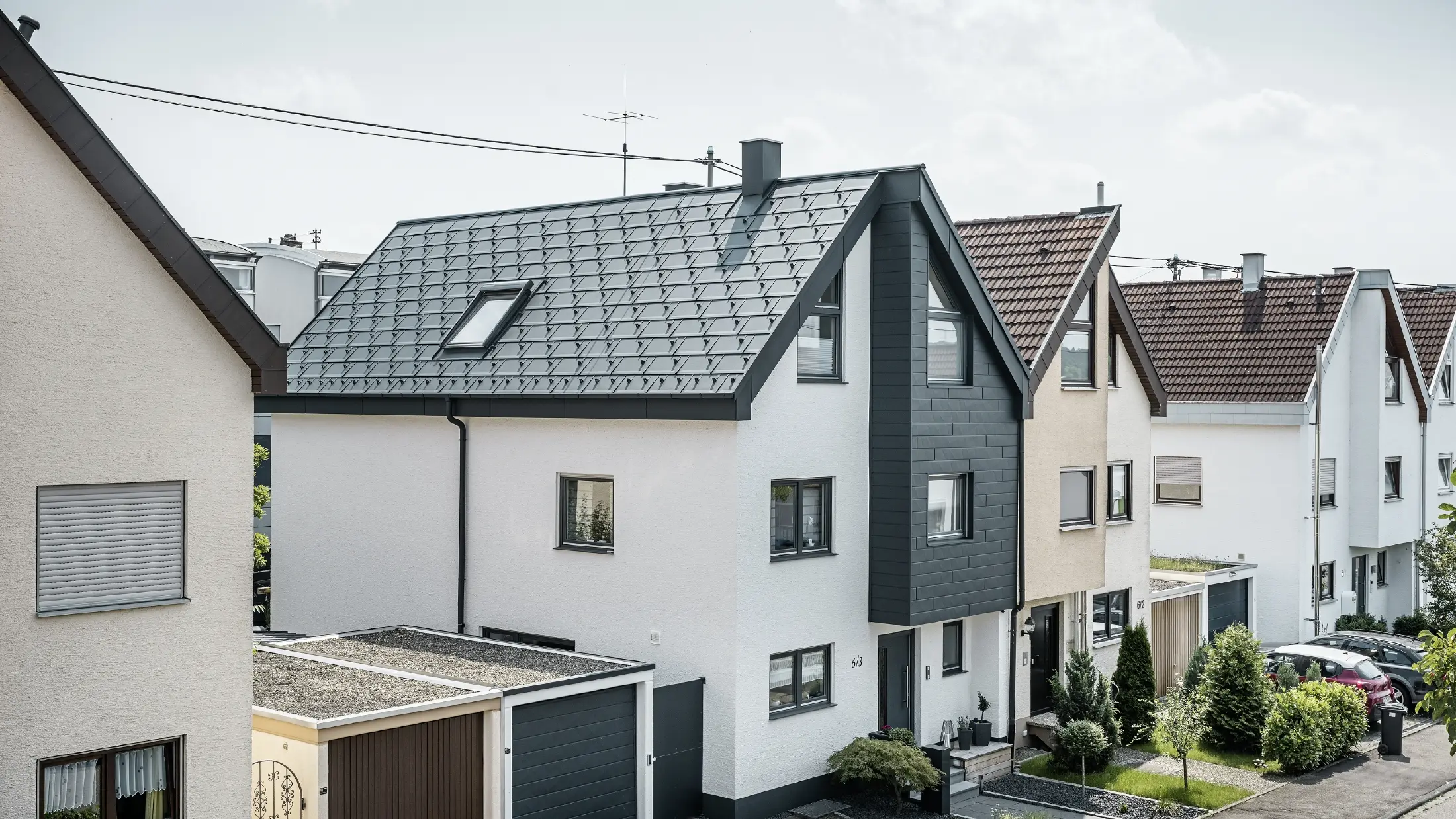 Eine Doppelhaushälfte wurde bereits saniert, mit frischer weißer Putzfassade, kombiniert mit einer PREFA Siding.X Fassade in Anthrazit. Das Dach wurde mit der PREFA Dachplatte R.16 eingedeckt. Die Dachentwässerung erfolgt über die eckige Kastenrinne inklusive PREFA Ablaufrohr.