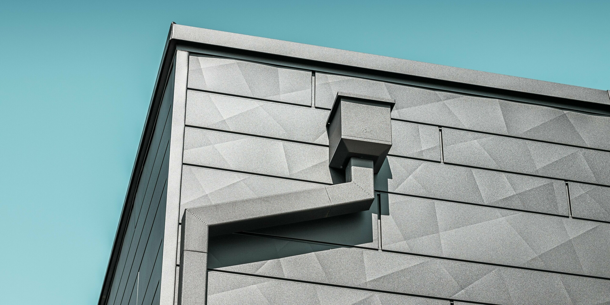 Die Fassade des sanierten Einfamilienhauses in Teuschnitz zieren PREFA Siding.X Aluminiumpaneele in der Farbe P.10 Schwarz mit ihrer einzigartigen, geometrischen Textur. Der Wasserfangkasten und das Quadratrohr von PREFA fügen sich elegant in das Design ein und bieten eine funktionale Lösung für die Entwässerung. Die präzise Verarbeitung und die harmonische Integration der Elemente unterstreichen die ästhetische Qualität und Langlebigkeit der PREFA Aluminiumprodukte.