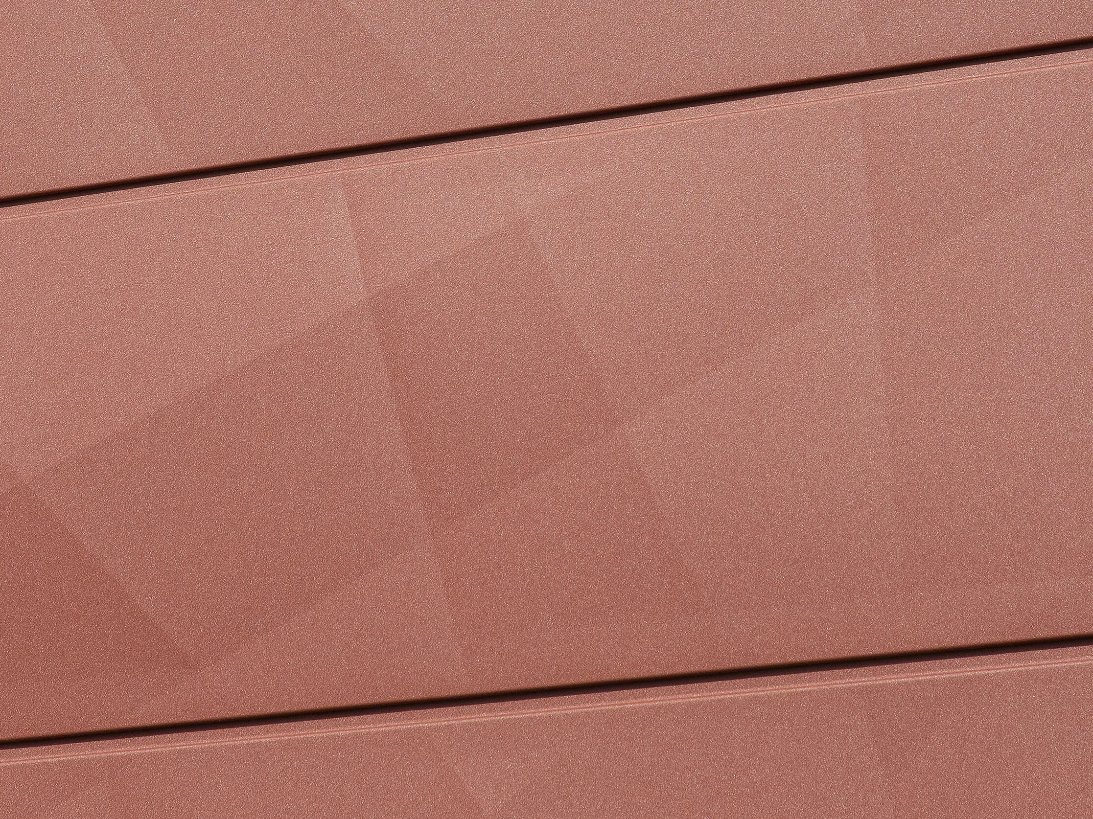 Detailaufnahme der PREFA Fassadenpaneele FX.12 in Oxydrot: Die prägnante Kantung erzeugt eine spannende geometrische Struktur, die das Licht je nach Tageszeit anders reflektiert. Die hochwertige Pulverbeschichtung in P.10 Qualität sorgt für dauerhafte Farbbrillanz und höchste Widerstandsfähigkeit – ideal für langlebige, wartungsfreie Fassadensanierungen.