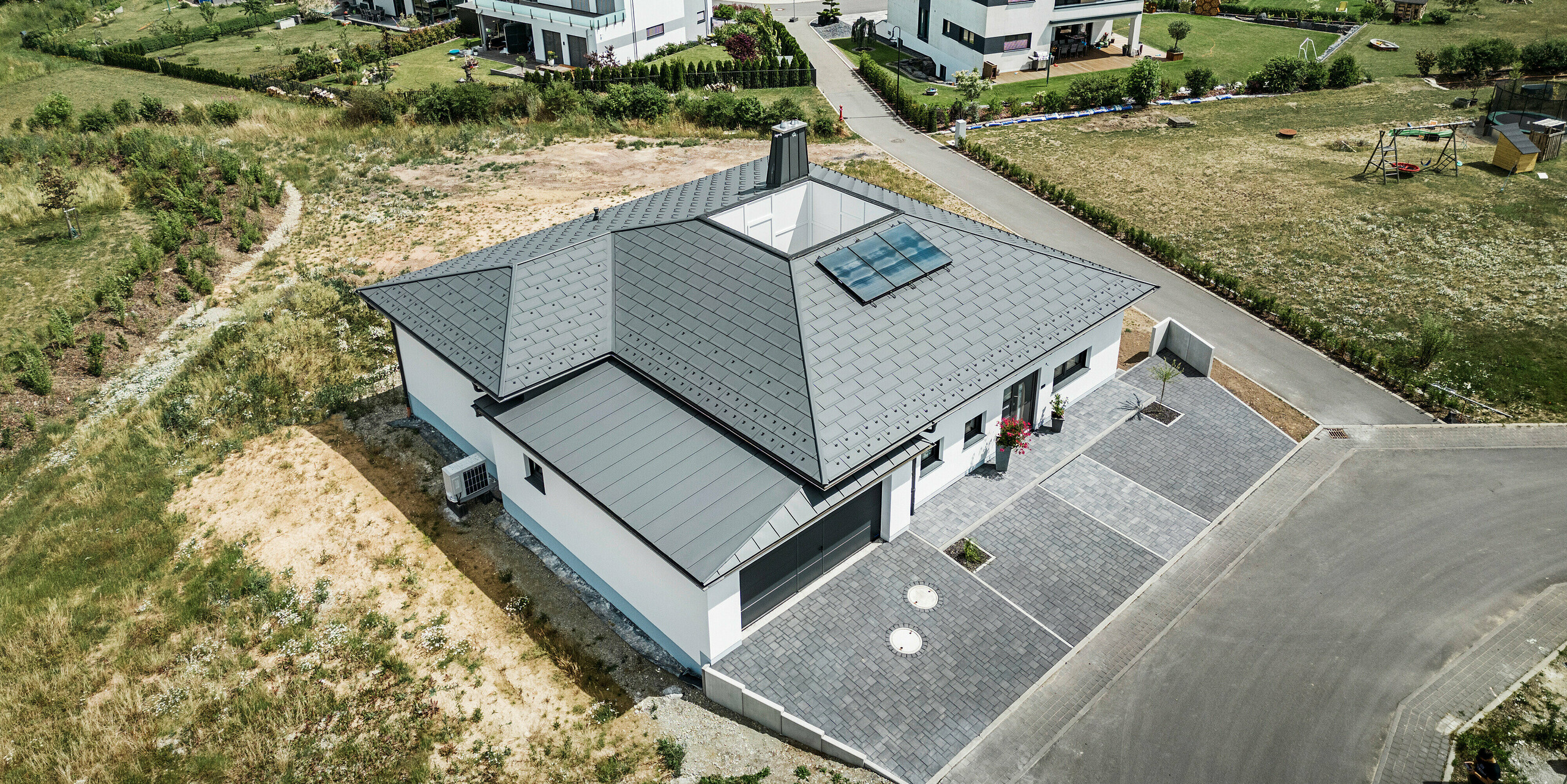 PREFA Dachplatte R.16 und PREFALZ sowie Ablaufrohr und Hängerinne in P.10 Dunkelgrau auf dem Dach eines Bungalows