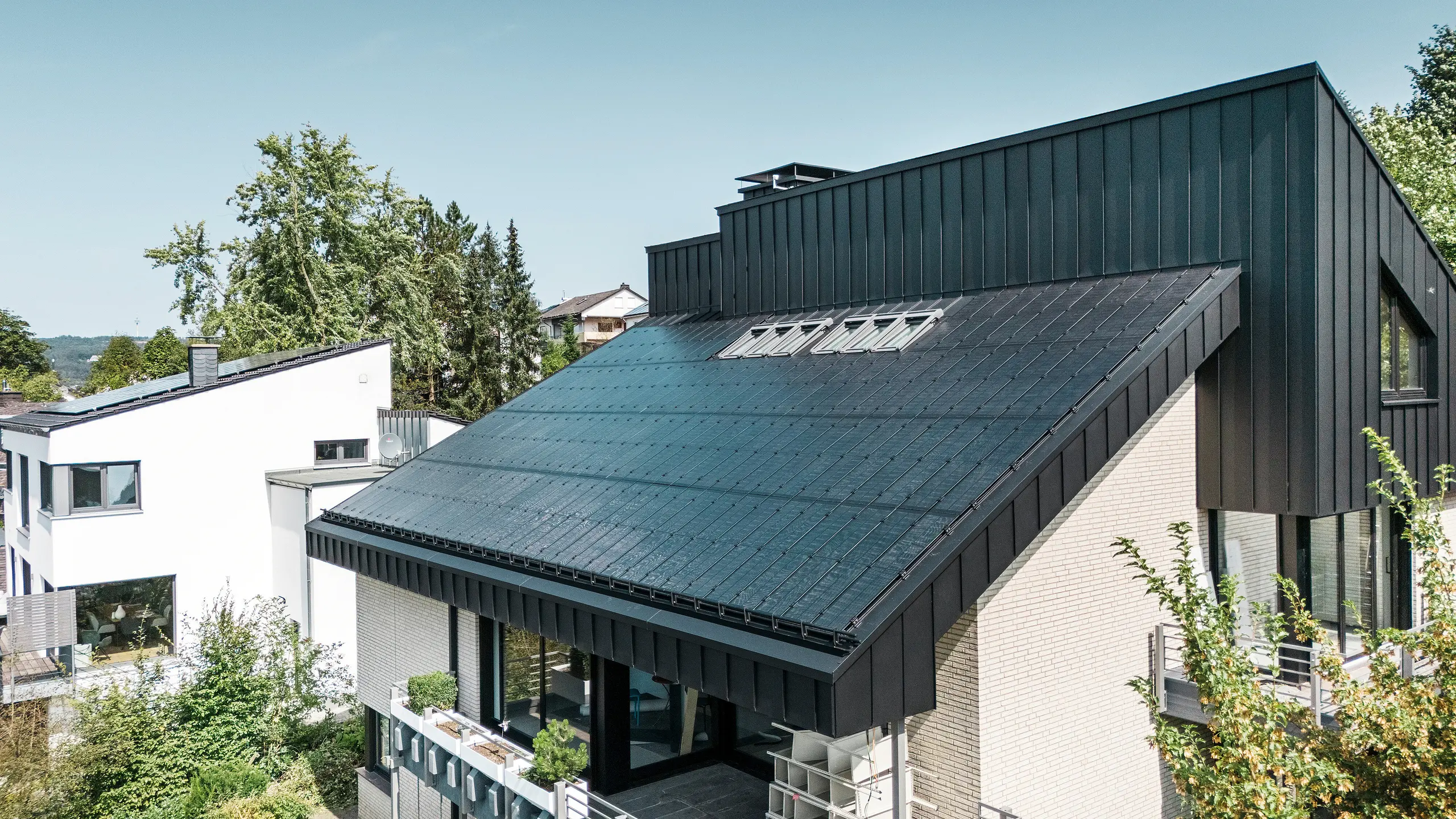 Moderne Architektur eines Einfamilienhauses in Meschede, Deutschland, mit einem PREFALZ-Aluminiumdach in P.10 Schwarz und integrierten Glas/Glas-Photovoltaikmodulen. Das versetzte Dach vereint zeitloses Design mit nachhaltiger Photovoltaik-Technologie. Die innovativen PREFALZ-Solarmodule liefern eine Leistung von 18 kWp. Die rahmenlosen Module und die elegante Aluminium-Dach- und Fassadenverkleidung bilden ein ästhetisches und funktionales Ganzes, das sich harmonisch in die grüne Wohnumgebung einfügt.