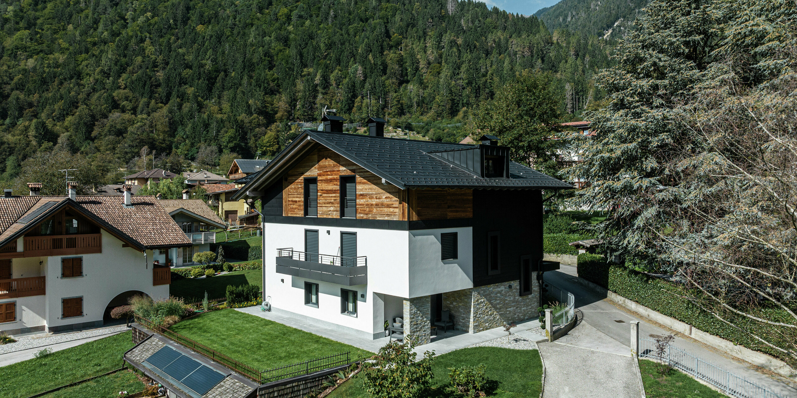 Modernes Wohnhaus in Pelugo, Italien, nach Renovierung und energetischer Sanierung. Das Dach wurde mit der widerstandsfähigen PREFA Dachplatte R.16 in P.10 Anthrazit eingedeckt, die Fassade erhielt mit PREFA Siding.X in P.10 Anthrazit eine moderne und langlebige Optik. Die Kombination von Aluminium, Holz und Putz schafft eine harmonische und witterungsbeständige Architektur.