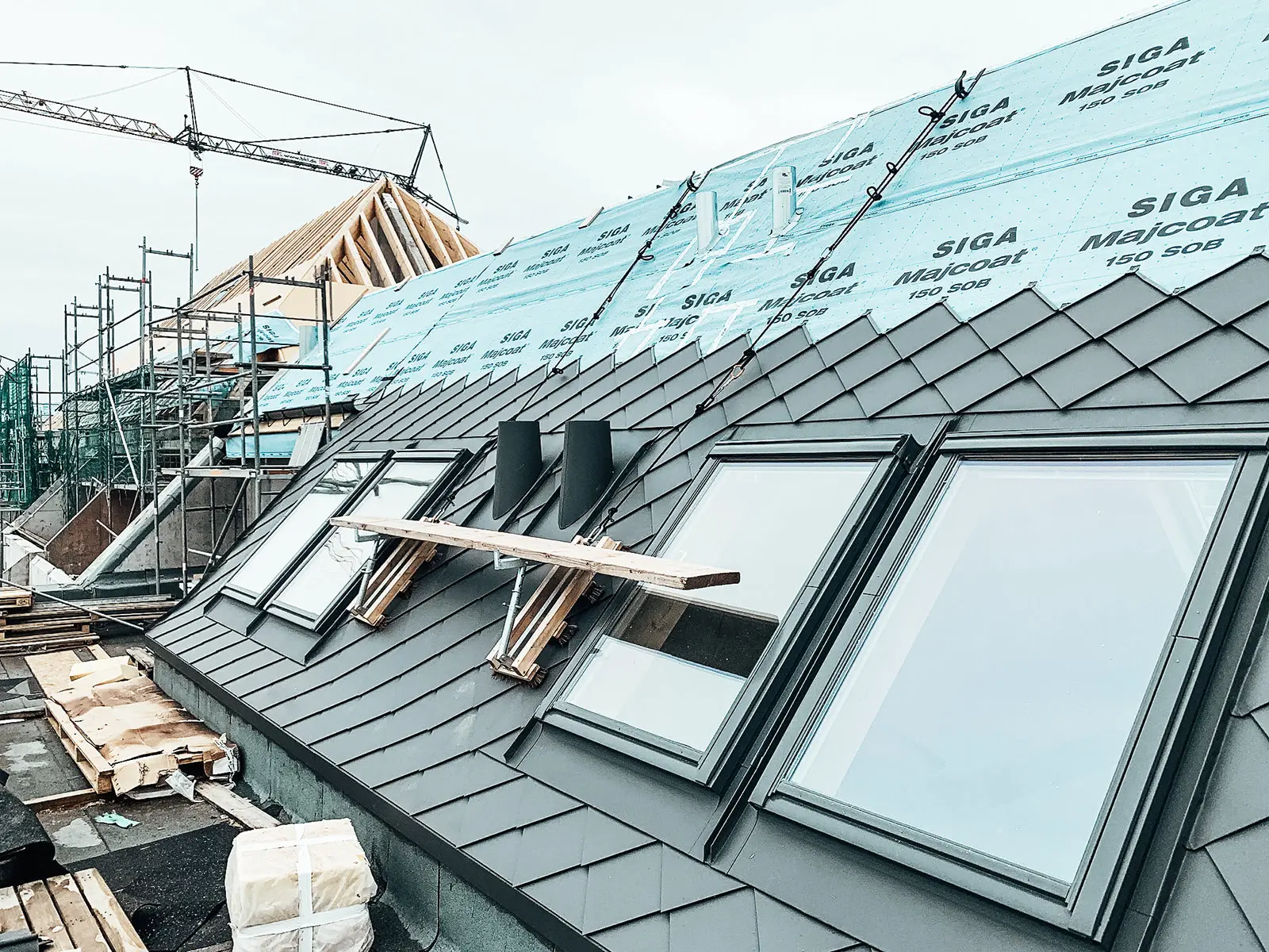 Sie können das Dach während der Renovierung sehen. Hier werden die rautenförmigen PREFA-Fassadenziegel 29x29 in P.10 dunkelgrau verlegt.